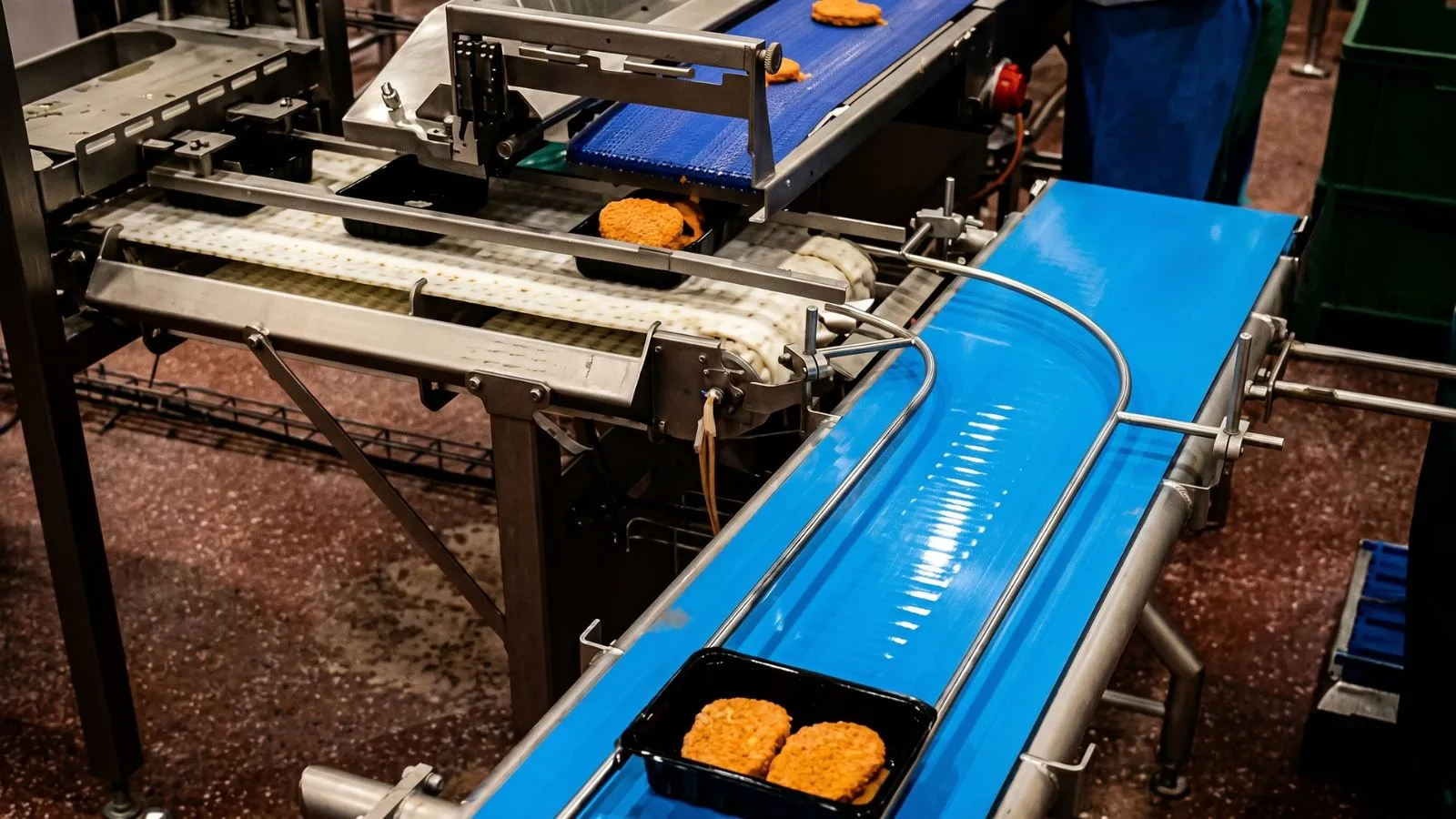Panierte Produkte laufen auf einem blauen Förderband durch die Produktion